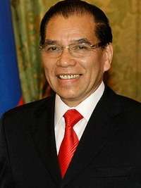 a happy-looking man with greying black hair, wearing a suit and tie