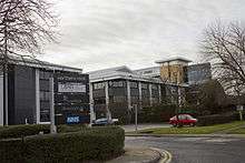 A number of black/grey buildings and taller sandstone and glass building, used as the headquarters of the Northern Rock bank