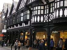 A terrace of shops with a covered walkway at ground level and timber framing above