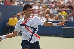 A brown-haired male tennis player with a white shirt and blue shorts