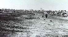 In the distance a group of people walk down a dirt road away from the village.