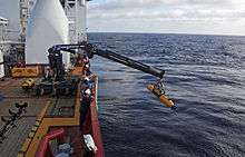 Crane lowering the torpedo-shaped Bluefin 21 into the water off the side of the Ocean Shield.