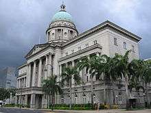 A dome sits atop this building, which is next to a road. The building's large entrance stands at its centre and is fronted with pillars.