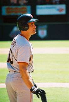 Baseball player, wearing a grey jersey with a black helmet, turning to his right