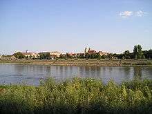 a colour photograph looking across a river at old buildings