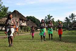 Four women, in colorful skirts, and a child outdoors