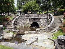 A decorative stone bridge, with curving stairs down to the water below on either side, in a park