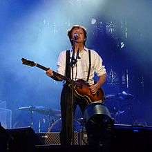 McCartney on stage playing guitar and singing.