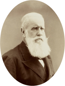 Half-length photographic portrait of an older man with white hair and beard dressed in a dark jacket and necktie