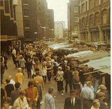 Colour photograph of a moderately crowded street, with stalls along one side.