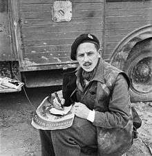 Philip John Gardner poses for a photograph, while he is seat looking slightly up at the camera while writing.