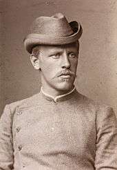 Portrait of a youngish man recognisable as Nansen from the earlier photograph. He has a stern expression and is wearing a collarless jacket buttoned to the neck.