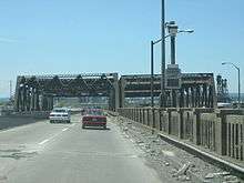 A four lane divided road on a truss bridge with another truss bridge visible to the right