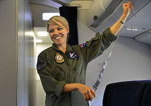  Woman in olive-green fatigues holding passenger oxygen mask in aircraft cabin