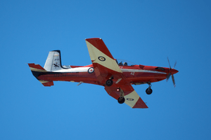 Single-engined military monoplane, painted red and white, in flight with wheels down