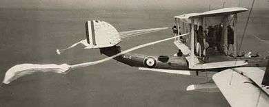 Two men holding outer struts of triple-finned flying boat with parachutes trailing behind