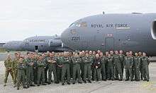 A group of people wearing overalls standing together in front of three large grey aircraft.