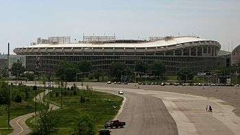  A large circular stadium with a curving overhang behind a mostly unused parking lot.