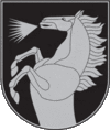 A coat of arms depicting a silver horse that is rearing and neighing all on a dark green background bordered by a thin silver line