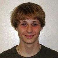 A young man smiling wearing a t-shirt and a golden necklace