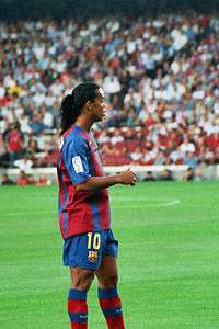 Isolated football player on the pitch, wearing the number 10 jersey. Vaguely smiling.