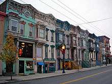 A row of attached brick three-story houses with pedimented roofs and elaborate decoration, painted in a variety of colors.