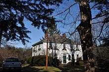 A large two story colonial frame house, five windows wide and three deep. It has a hip roof and two chimneys. The second floor windows have Christmas greenery below them, and the word Noel has been hung below the central window and above the front door.