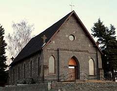 Photograph of a small stone church sitting prominently on a small rise.