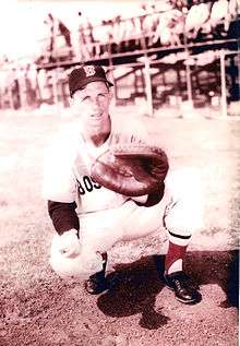 A black-and-white image of a crouching man holding a catcher's mitt extended