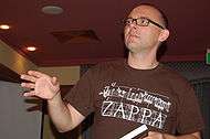 A man with the shot focused on his upper body. He is wearing a pair of glasses and a brown shirt.