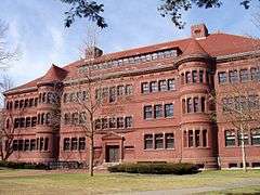 A large brick academic building. It has some ornate decorations, and two rounded sections separate the central portion from wings on either side.