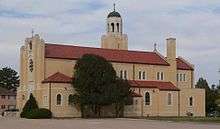 Brick church with Mission-style tile roof; square tower surmounted with cross-topped dome