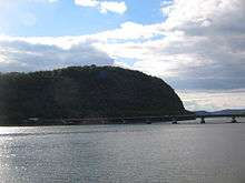 A concrete highway bridge crosses a large river in front of a tall wooded bluff