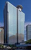 Ground-level view of a blue, glass, rectangular high-rise lined with rows of windows; a small circular pad sits atop the building