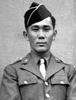 Head and shoulders of a young man standing erect, wearing a garrison cap and a military jacket over a shirt and tie.