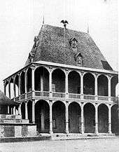 Large two-storey wood building with decoratively carved verandas supported by tall pillars