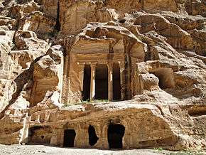 A colonnades classically styled temple carved out of a beige-colored rock cliff face.