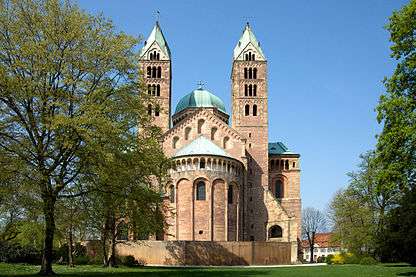 Looking toward the choir of a brick Romanesque cathedral. The twin bell towers, the transept crossing dome, and the roof are green copper.