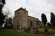 A stone church seen from the southwest, in the foreground a large, squat tower with a pyramidal roof, and the body of the church extending behind it