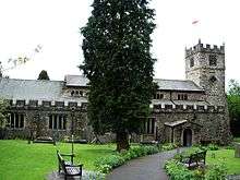 A long stone church see from the north, with a clerestory, a battlemented parapet along the aisle, and a west tower