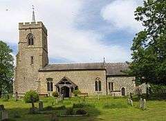 ancient stone village church with tower, in graveyard surrounded by trees