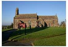 A simple, small, stone church with a west bellcote seen from the south