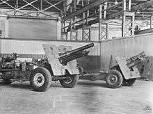 Two artillery guns mounted on wheeled gun carriages photographed inside of a building. The weapons have a large plate mounted about half way down the length of their barrels.