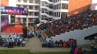 Audience in outdoor bleachers in front of a stage