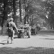 Men on foot and jeeps towing guns on a tree lined road