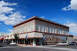 Photograph of a 2-story commercial building standing on a street corner, with a storefront on one side and a mural on another