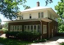 Two-story house with low-pitched roof; brick below, clapboard above