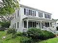 A white colonial frame house with a wide single story front porch. The main rectangle of the house has extensions to the rear.