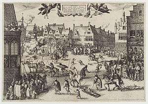 A busy urban scene. Medieval buildings surround an open space, in which several men are being dragged by horses. One man hangs from a scaffold. A corpse is being hacked into pieces. Another man is feeding a large cauldron with a dismembered leg.  Thousands of people line the streets and look from windows.  Children and dogs run freely.  Soldiers keep them back.