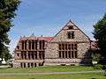 This building is made of granite with brownstone trim, and a red roof. Vertical window structures dominate the wall that is shown. On the right the roof has a large gable, and there are three smaller gable ends on the left.